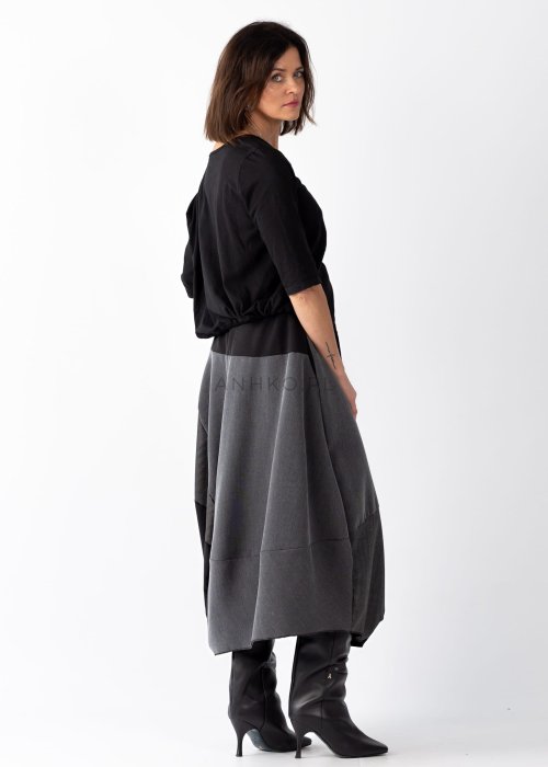 Czarna bluzka damska z asymetrycznym dekoltem odsłaniającym ramię i guzikami, stylizowana z elegancką spódnicą w minimalistycznym looku.