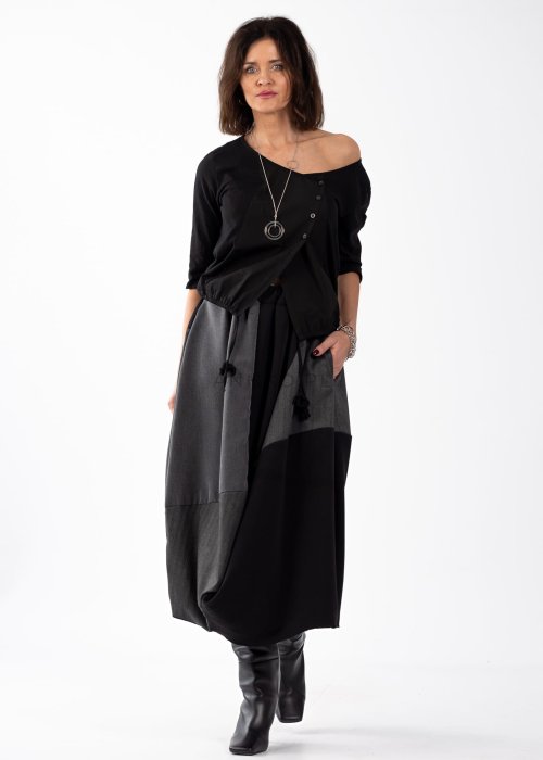 Czarna bluzka damska z asymetrycznym dekoltem odsłaniającym ramię i guzikami, stylizowana z elegancką spódnicą w minimalistycznym looku.