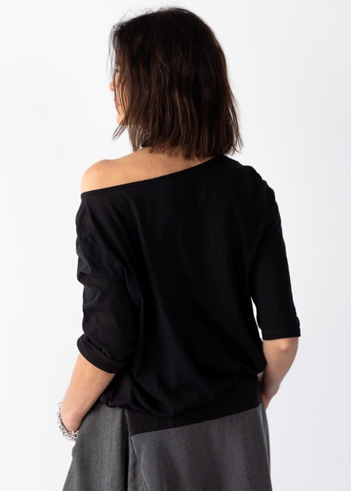 Czarna bluzka damska z asymetrycznym dekoltem odsłaniającym ramię i guzikami, stylizowana z elegancką spódnicą w minimalistycznym looku.