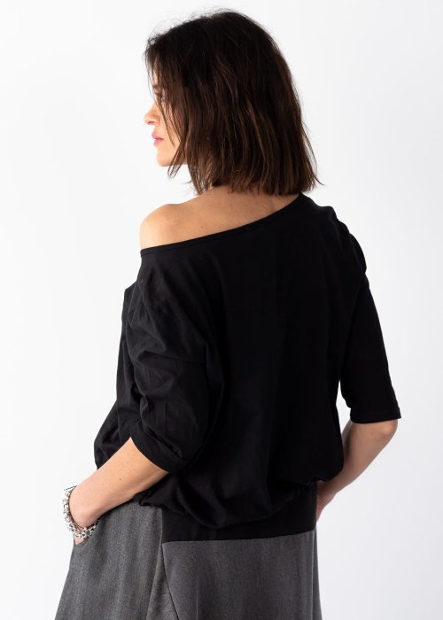 Czarna bluzka damska z asymetrycznym dekoltem odsłaniającym ramię i guzikami, stylizowana z elegancką spódnicą w minimalistycznym looku.