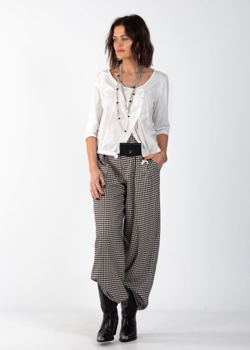 Biała bluzka damska z guzikami i regulowanym dołem, o minimalistycznym kroju, stylizowana z wzorzystą spódnicą i biżuterią w eleganckim looku.