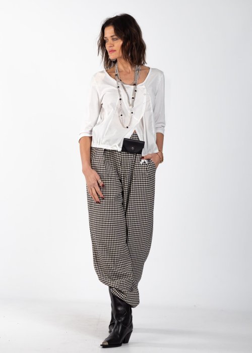 Biała bluzka damska z guzikami i regulowanym dołem, o minimalistycznym kroju, stylizowana z wzorzystą spódnicą i biżuterią w eleganckim looku.