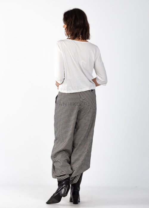 Biała bluzka damska z guzikami i regulowanym dołem, o minimalistycznym kroju, stylizowana z wzorzystą spódnicą i biżuterią w eleganckim looku.