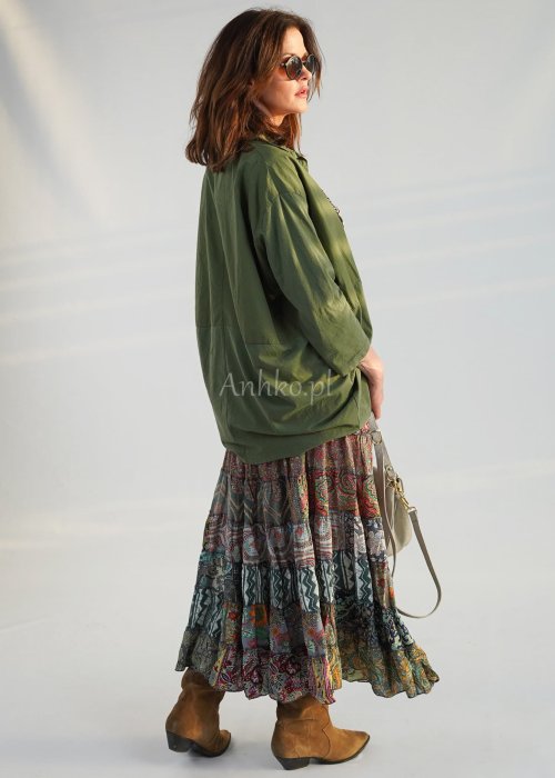 Khaki koszula damska oversize z kołnierzykiem i przeszyciem poniżej biustu, zestawiona z wzorzystą spódnicą maxi i botkami w stylizacji casual.
