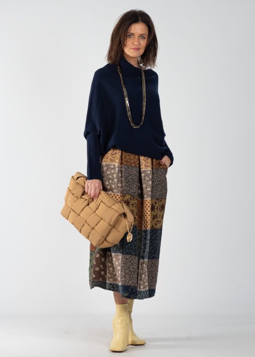 Granatowy sweter damski oversize o nietoperzowym kroju z asymetrycznym dołem, stylizacja z wzorzystą spódnicą i biżuterią.