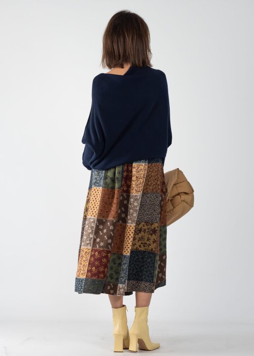 Granatowy sweter damski oversize o nietoperzowym kroju z asymetrycznym dołem, stylizacja z wzorzystą spódnicą i biżuterią.