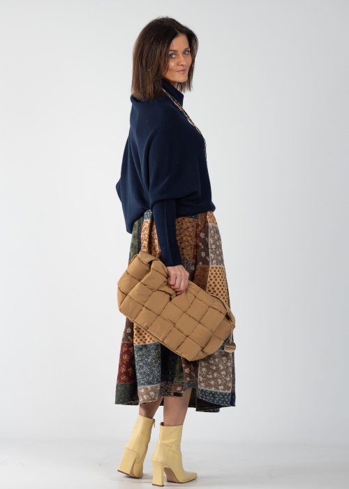 Granatowy sweter damski oversize o nietoperzowym kroju z asymetrycznym dołem, stylizacja z wzorzystą spódnicą i biżuterią.