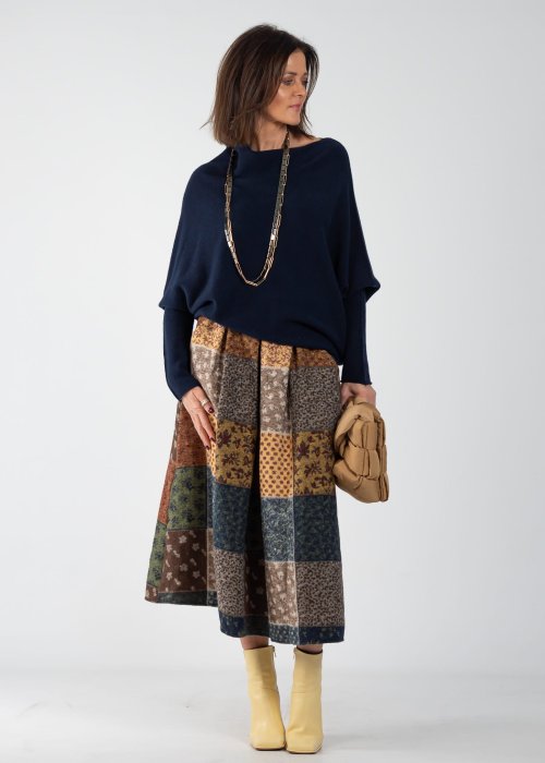 Granatowy sweter damski oversize o nietoperzowym kroju z asymetrycznym dołem, stylizacja z wzorzystą spódnicą i biżuterią.