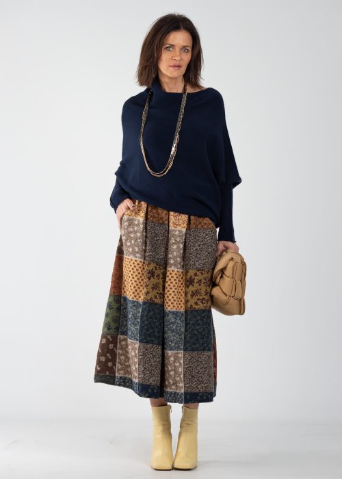 Granatowy sweter damski oversize o nietoperzowym kroju z asymetrycznym dołem, stylizacja z wzorzystą spódnicą i biżuterią.