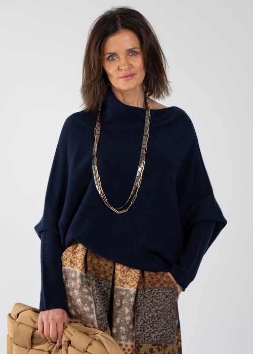 Granatowy sweter damski oversize o nietoperzowym kroju z asymetrycznym dołem, stylizacja z wzorzystą spódnicą i biżuterią.