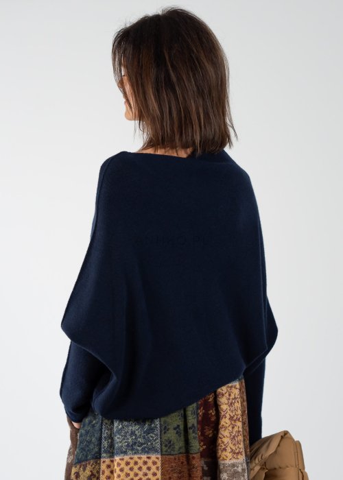Granatowy sweter damski oversize o nietoperzowym kroju z asymetrycznym dołem, stylizacja z wzorzystą spódnicą i biżuterią.