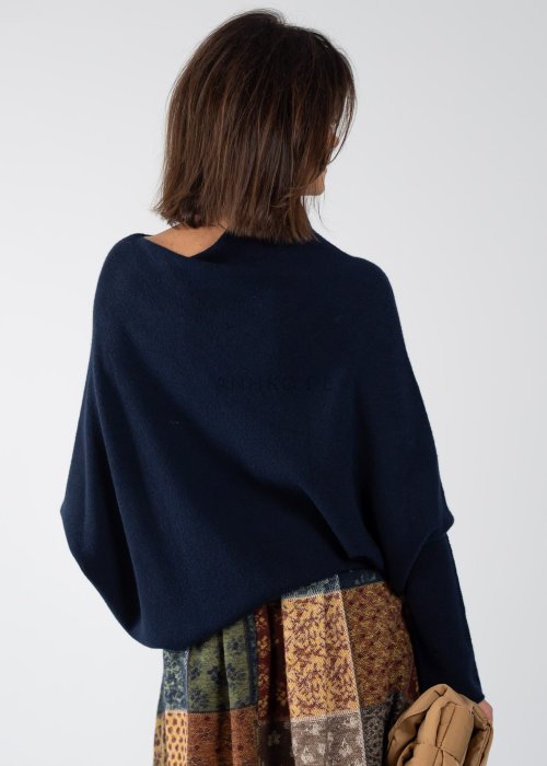 Granatowy sweter damski oversize o nietoperzowym kroju z asymetrycznym dołem, stylizacja z wzorzystą spódnicą i biżuterią.