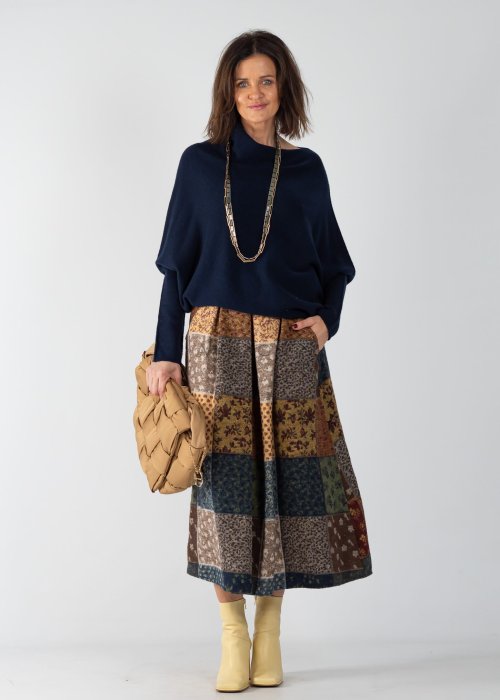 Granatowy sweter damski oversize o nietoperzowym kroju z asymetrycznym dołem, stylizacja z wzorzystą spódnicą i biżuterią.
