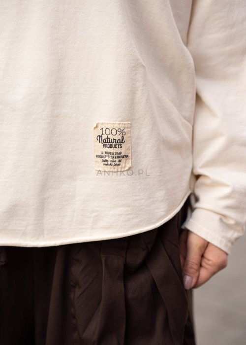 Śmietankowa bluza damska oversize z długim rękawem i naszywką na froncie. Luźny fason w stylizacji z szerokimi spodniami w miejskim stylu.