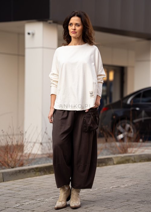 Śmietankowa bluza damska oversize z długim rękawem i naszywką na froncie. Luźny fason w stylizacji z szerokimi spodniami w miejskim stylu.