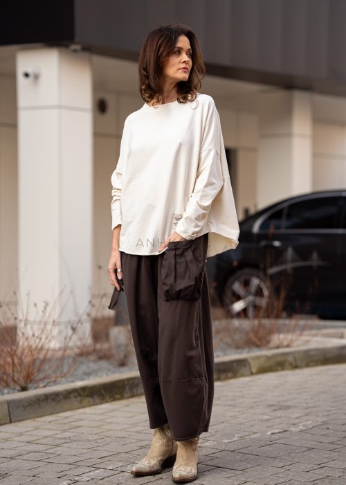 Śmietankowa bluza damska oversize z długim rękawem i naszywką na froncie. Luźny fason w stylizacji z szerokimi spodniami w miejskim stylu.