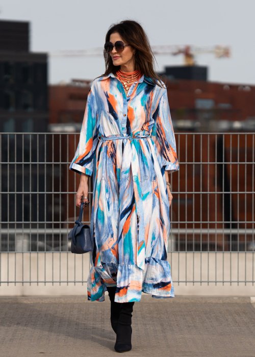 Sukienka maxi w artystyczny print w odcieniach błękitu, pomarańczu i granatu z efektownym wiązaniem w talii. Zwiewny fason z falbaną przy dole oraz koszulową górą nadaje sylwetce lekkości i elegancji.