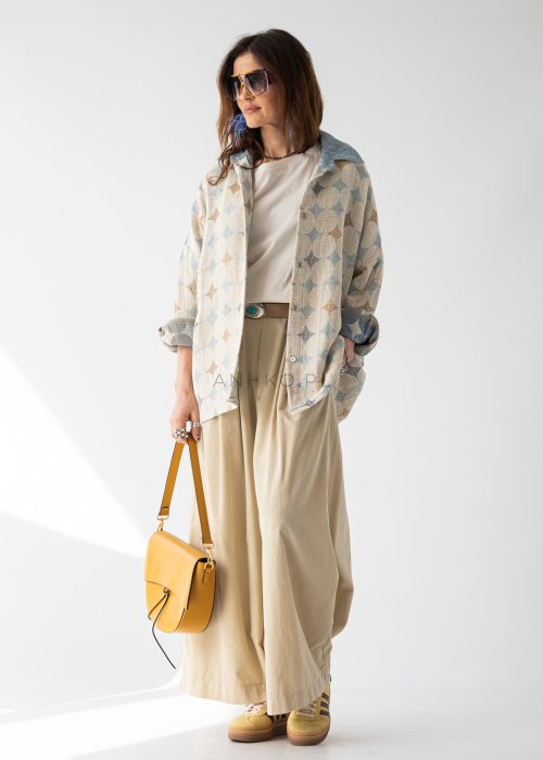 Kremowa bluzka damska oversize z szerokim dekoltem i krótkim rękawem w stylizacji z beżowymi spodniami i paskiem.