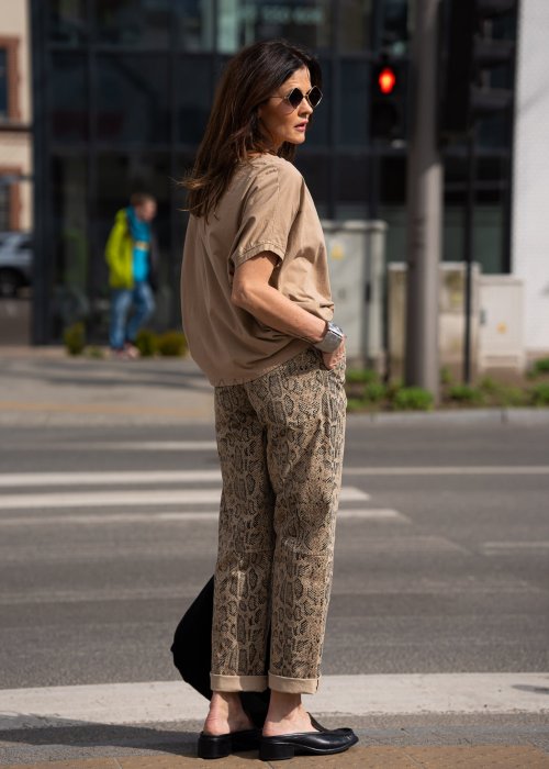 Bluzka damska w odcieniu camel z szerokim dekoltem i krótkim rękawem, zestawiona ze spodniami w zwierzęcy wzór w miejskiej stylizacji.