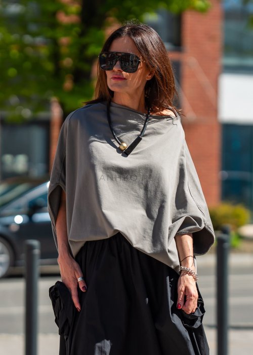 Bluzka damska taupe oversize z rękawami typu nietoperz i opadającym dekoltem, zestawiona z czarną spódnicą. Minimalistyczna stylizacja miejska.