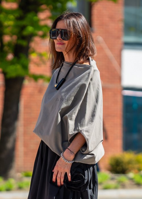 Bluzka damska taupe oversize z rękawami typu nietoperz i opadającym dekoltem, zestawiona z czarną spódnicą. Minimalistyczna stylizacja miejska.