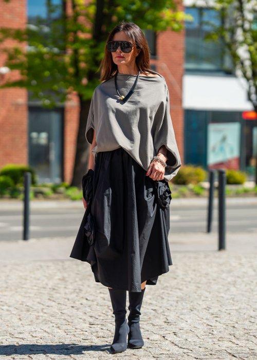Bluzka damska taupe oversize z rękawami typu nietoperz i opadającym dekoltem, zestawiona z czarną spódnicą. Minimalistyczna stylizacja miejska.