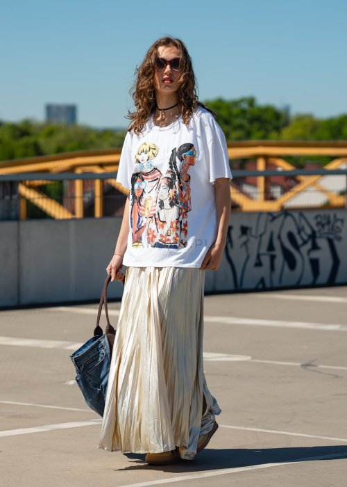 Biała bluzka damska t-shirt z kolorowym nadrukiem postaci i kwiatów, o luźnym kroju, w stylizacji miejskiej z plisowaną spódnicą.