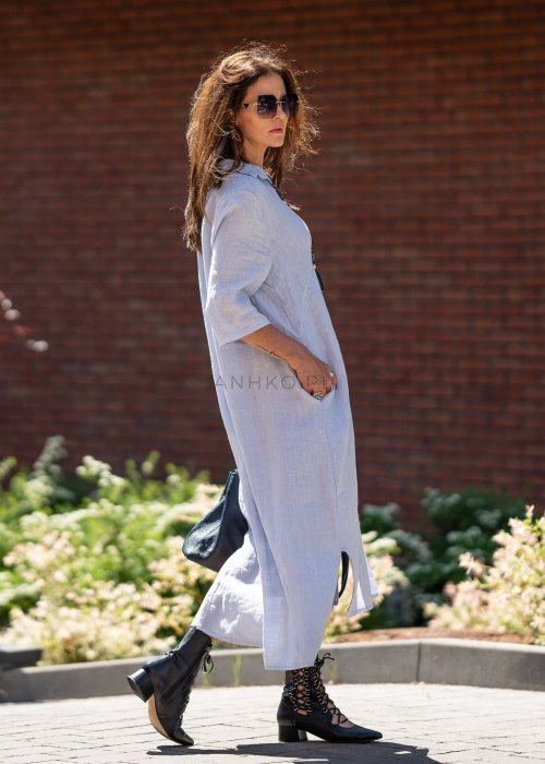 Jasnoniebieska lniana sukienka maxi w stylu szmizjerki, zapinana na guziki, z luźnym fasonem i kołnierzykiem, stylizowana z czarnymi botkami i torebką.