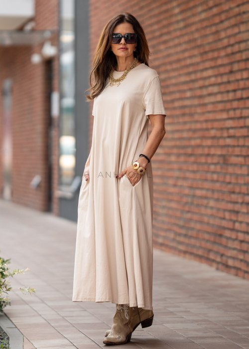Beżowa sukienka maxi o luźnym kroju z krótkim rękawem i kieszeniami po bokach. Model pokazany w stylizacji z kowbojkami i złotą biżuterią.