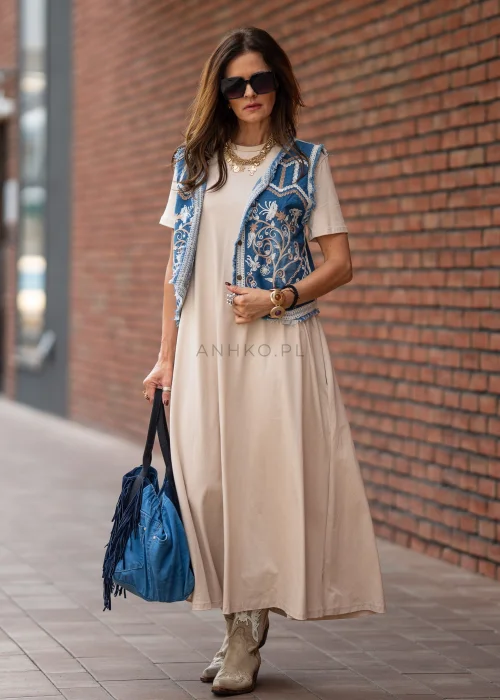Beżowa sukienka maxi o luźnym kroju z krótkim rękawem i kieszeniami po bokach. Model pokazany w stylizacji z kowbojkami i złotą biżuterią.