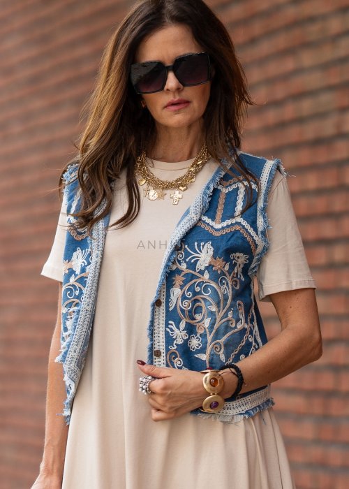Niebieska kamizelka jeansowa damska z bogatymi haftami i surowym wykończeniem. Stylizacja z beżową sukienką i biżuterią w stylu boho.