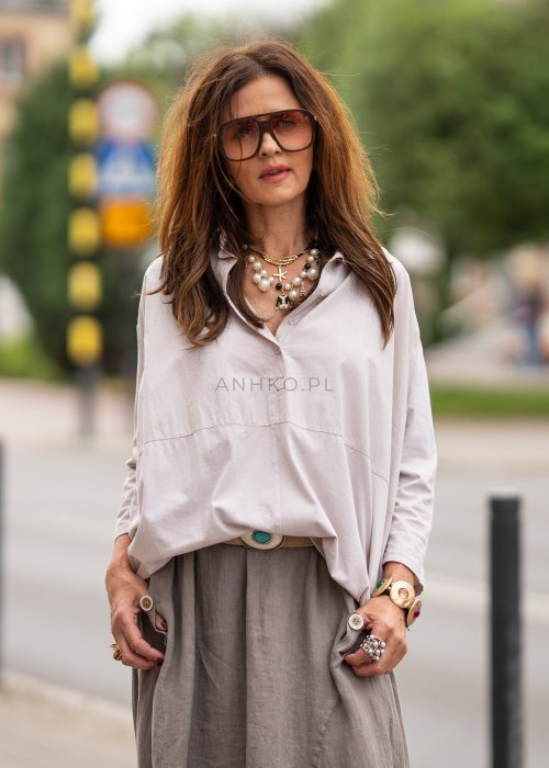 Beżowa koszula oversize z kołnierzem i zapięciem na guziki, o luźnym fasonie i subtelnym przeszyciu z przodu. Stylizacja w neutralnych, naturalnych tonach.