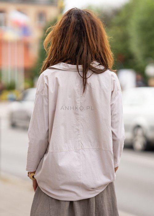 Beżowa koszula oversize z kołnierzem i zapięciem na guziki, o luźnym fasonie i subtelnym przeszyciu z przodu. Stylizacja w neutralnych, naturalnych tonach.