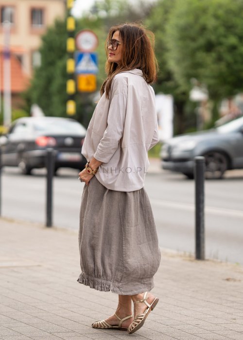 Beżowa koszula oversize z kołnierzem i zapięciem na guziki, o luźnym fasonie i subtelnym przeszyciu z przodu. Stylizacja w neutralnych, naturalnych tonach.