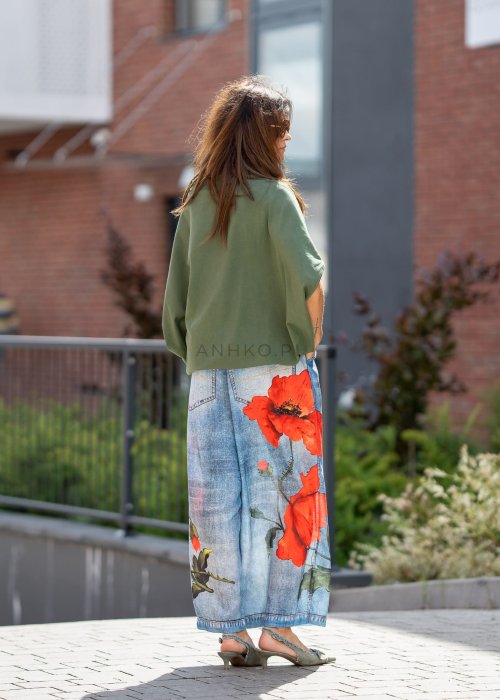 Ciemnozielona bluzka oversize z szerokim rękawem typu nietoperz i opadającym dekoltem, zestawiona z jeansami z czerwonym printem w miejskiej stylizacji.