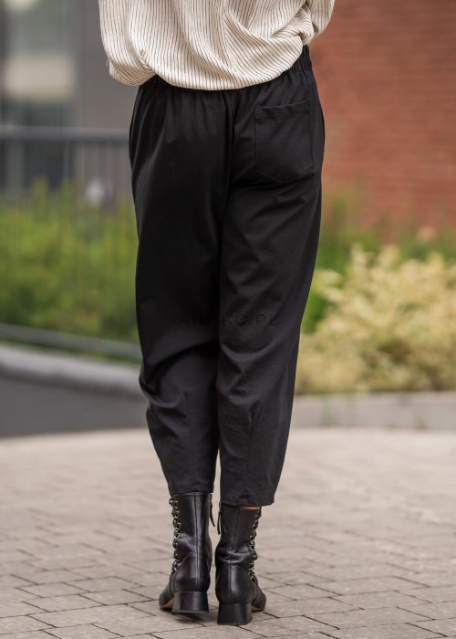 Czarne spodnie damskie typu cygaretki z elastycznym pasem i zwężaną nogawką, zestawione z botkami w eleganckiej miejskiej stylizacji.