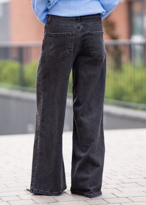 Czarne damskie jeansy z prostą, lekko rozszerzaną nogawką, klasyczny krój z pięcioma kieszeniami i zapięciem na guzik, noszone z białymi sneakersami.