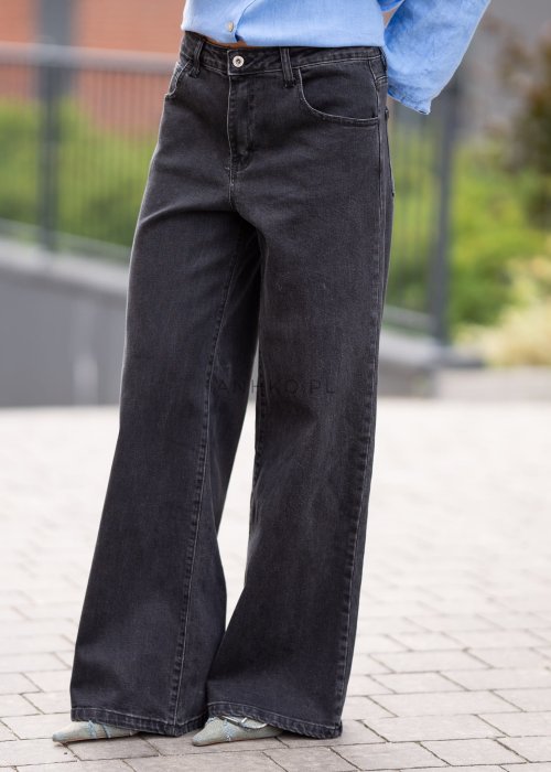 Czarne damskie jeansy z prostą, lekko rozszerzaną nogawką, klasyczny krój z pięcioma kieszeniami i zapięciem na guzik, noszone z białymi sneakersami.