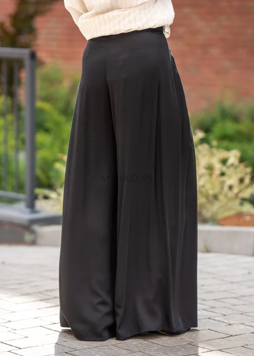 Eleganckie spodnie damskie w kolorze czarnym, z wysokim stanem, szerokimi nogawkami typu palazzo, zakładkami przy talii i asymetrycznym, kopertowym wykończeniem pasa.