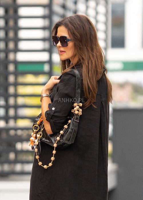 Czarna lniana sukienka maxi w stylu szmizjerki, zapinana na guziki, o luźnym fasonie oversize, stylizowana z sandałami i torebką.