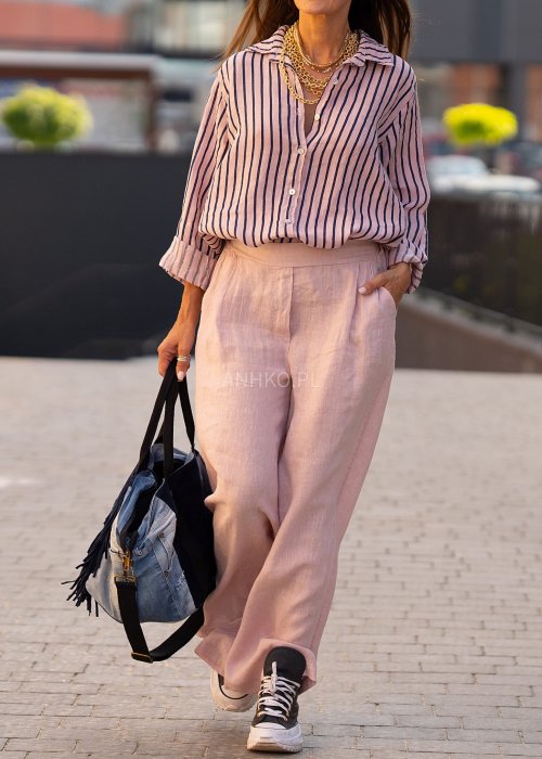 Lniana koszula damska w różowym kolorze z granatowymi paskami, luźny fason z kołnierzykiem i guzikami, stylizacja z jasnymi spodniami.