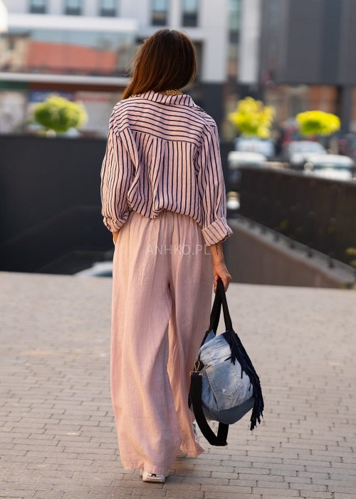 Lniana koszula damska w różowym kolorze z granatowymi paskami, luźny fason z kołnierzykiem i guzikami, stylizacja z jasnymi spodniami.