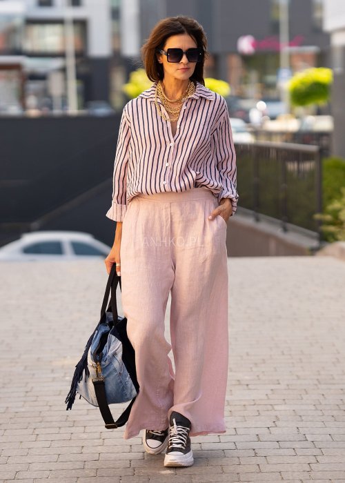 Lniana koszula damska w różowym kolorze z granatowymi paskami, luźny fason z kołnierzykiem i guzikami, stylizacja z jasnymi spodniami.