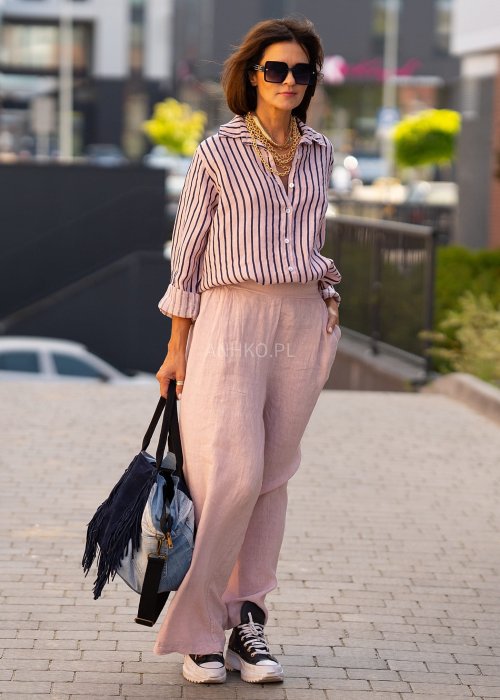 Lniana koszula damska w różowym kolorze z granatowymi paskami, luźny fason z kołnierzykiem i guzikami, stylizacja z jasnymi spodniami.