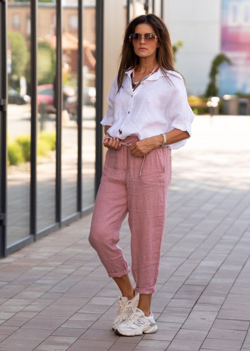 Jasnoróżowe lniane spodnie damskie z gumą w pasie i kieszeniami, model o swobodnym kroju stylizowany z białą koszulą i sneakersami.