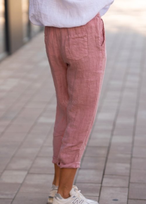 Jasnoróżowe lniane spodnie damskie z gumą w pasie i kieszeniami, model o swobodnym kroju stylizowany z białą koszulą i sneakersami.