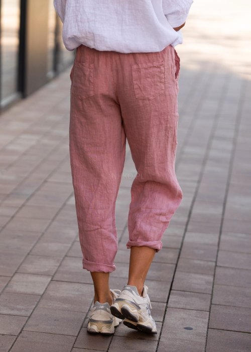 Jasnoróżowe lniane spodnie damskie z gumą w pasie i kieszeniami, model o swobodnym kroju stylizowany z białą koszulą i sneakersami.