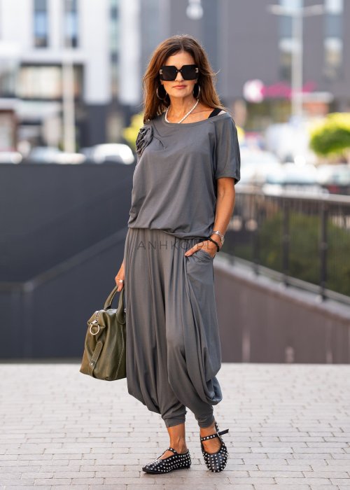 Grafitowa bluzka damska o luźnym kroju z dekoltem w łódkę i materiałowym kwiatem na ramieniu. Stylizacja z szerokimi spodniami w eleganckim, miejskim stylu.