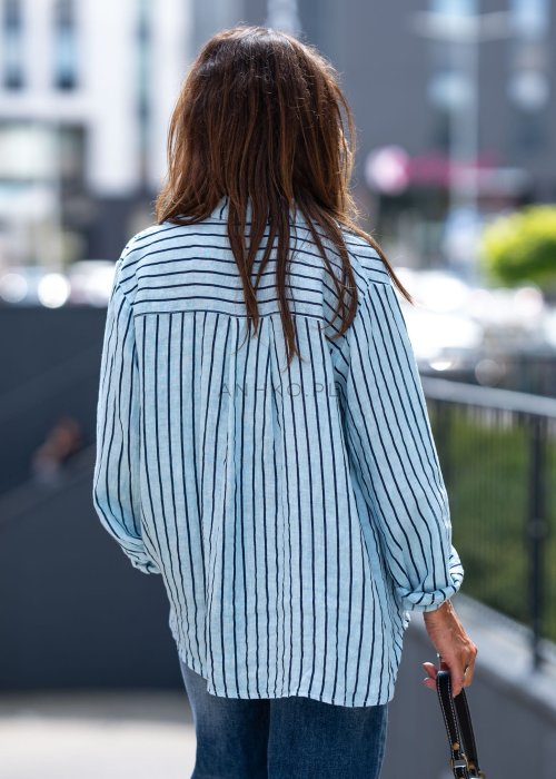 Lniana koszula damska niebieska w paski, luźny fason z kołnierzykiem i guzikami, stylizacja z jeansami i minimalistyczną biżuterią.