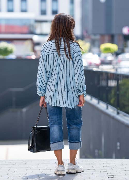 Lniana koszula damska niebieska w paski, luźny fason z kołnierzykiem i guzikami, stylizacja z jeansami i minimalistyczną biżuterią.